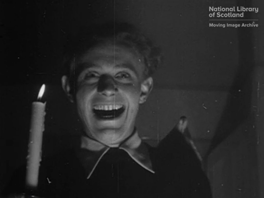 Black and white still of young man holding lit candle and laughing 